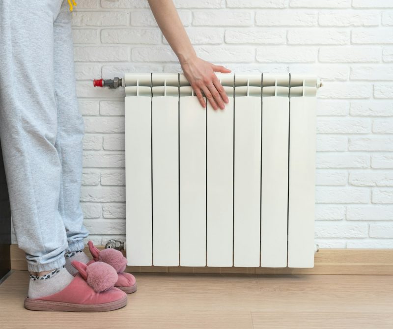 The girl keeps her hand on the heating radiator to check is turned on. Winter heating efficiency